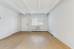 Bright and spacious living room with elegant wooden flooring, large window, and minimalistic white walls.