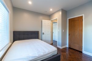 Inviting bedroom with a modern grey headboard, polished wooden floors, and soft natural light.