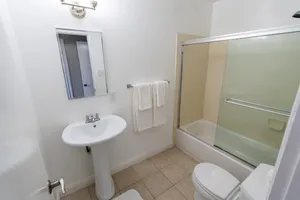 Modern bathroom with sleek pedestal sink, elegant glass shower doors, and bright tiling, creating a fresh and inviting space.