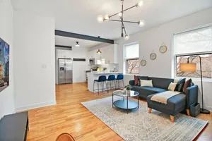 Contemporary open-concept living space featuring a stylish kitchen with bar seating, modern lighting, and a cozy living area with large windows.