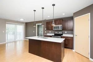 Modern kitchen with sleek countertops, stainless steel appliances, and elegant pendant lighting, opening to a bright living area with sliding glass doors.