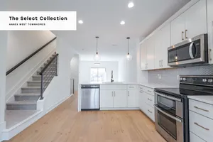 Sleek modern kitchen with stainless steel appliances, ample white cabinetry, and elegant pendant lighting in a spacious open-concept townhome.