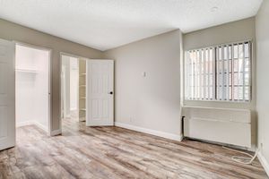 Spacious bedroom with elegant wood flooring, large window with blinds, and open closet doors.