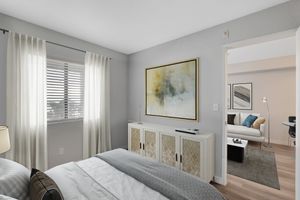 Cozy bedroom with elegant decor, soft sunlight through sheer curtains, and a glimpse into a modern living room with a stylish sofa.