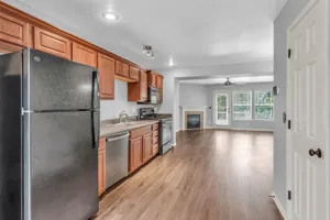 Modern open-concept kitchen with sleek wooden cabinets, stainless steel appliances, and bright, spacious living area featuring large windows and a cozy fireplace.