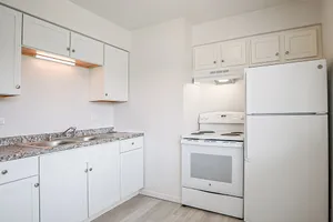 Bright, modern kitchen with sleek white cabinetry and granite countertops, featuring a spacious fridge and electric stove.