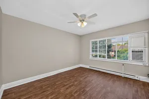 Bright, empty room with elegant wood flooring and a large window offering natural light, featuring a ceiling fan for optimal comfort.