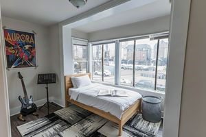 Bright bedroom showcasing a cozy single bed with modern decor, large windows offering ample sunlight, and a stylish music corner with a guitar and poster.