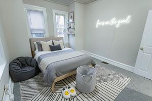 Inviting bedroom with plush bedding, chic neon wall art, and cozy bean bag chair accentuating a serene ambiance.