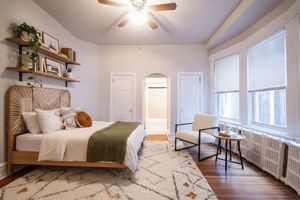 Inviting bedroom with plush bed, cozy chair, and warm natural light filtering through large windows.