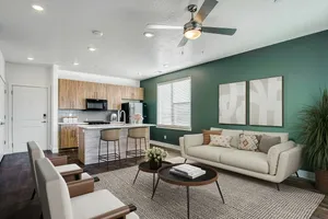 Modern living room featuring elegant open-concept kitchen with sleek wooden cabinets and cozy seating area, complemented by a stylish ceiling fan and decorative plants.