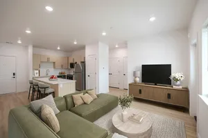 Modern open-concept living space featuring a cozy green sectional, stylish kitchen with light wood cabinets, and elegant decor.