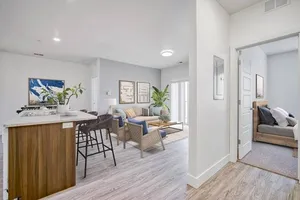Bright and modern open-concept apartment featuring a cozy living area, stylish kitchen with island seating, and a glimpse of a serene bedroom.
