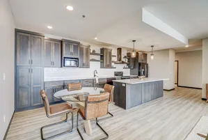 Sleek modern kitchen with dark cabinetry, stainless steel appliances, and open dining area featuring a glass-top table and leather chairs.