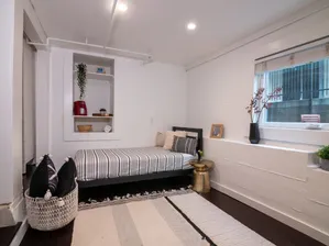 Cozy apartment bedroom with a modern design, featuring a stylish bed, decorative pillows, and a chic gold side table. Natural light streams through a large window, enhancing the elegant minimalist decor.