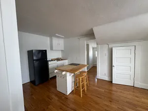 Charming kitchen area with wooden flooring, sleek black fridge, and cozy island with barstools for casual dining.