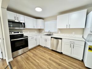Bright kitchen with sleek white cabinets, stainless steel appliances, and wooden flooring.