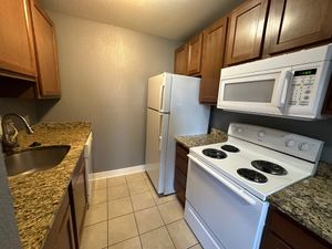 Compact kitchen with granite countertops, white appliances, and wood cabinetry.