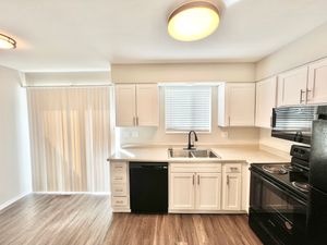 Bright modern kitchen with sleek white cabinets, black appliances, and wood flooring, featuring double sinks and ample counter space.