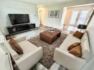 Modern living room with sleek white sofas, a large flat-screen TV, and elegant decor, showcasing a bright and inviting space with natural light.