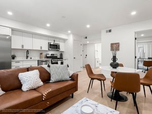 Modern open-concept living space featuring a sleek kitchen with stainless steel appliances, cozy brown leather sofa, and elegant dining area with a marble table.