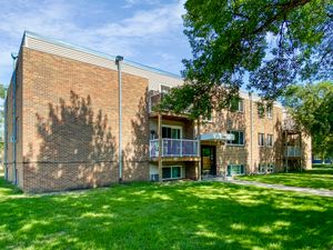 Charming brick apartment building with lush green lawn, shaded by mature trees, offering a serene and inviting atmosphere.
