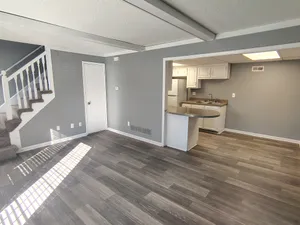 Modern open-plan living area with stylish laminate flooring, adjacent to a compact kitchen and elegant staircase.