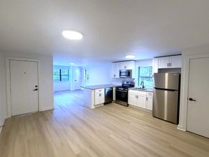 Bright, modern kitchen with stainless steel appliances, sleek white cabinets, and spacious open layout with new floors.