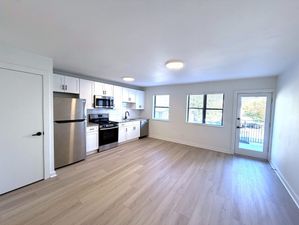 Bright, open-concept kitchen and living area with modern stainless steel appliances, sleek white cabinetry, and large windows providing ample natural light.