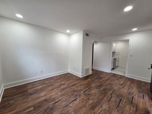 Inviting living space with elegant wood flooring and modern recessed lighting leading to a sleek kitchen area.
