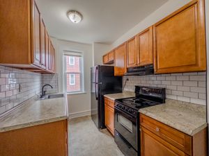 kitchen with wooden cabinets and tile backsplash, black fridge and oven/stove, apartment kitchen, lots of cabinets, facing window