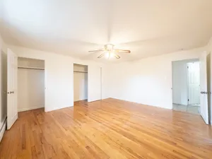 Spacious bedroom with pristine hardwood floors, dual closets, and a stylish ceiling fan, perfect for comfortable living.