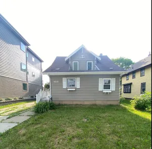 Charming two-story house with gray siding, featuring a green lawn and cozy front entrance.