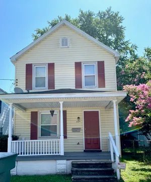 Charming two-story home with a welcoming front porch, vibrant shutters, and blooming garden scenery.