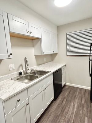 Contemporary kitchen with white cabinetry, marble countertops, and stainless steel sink.
