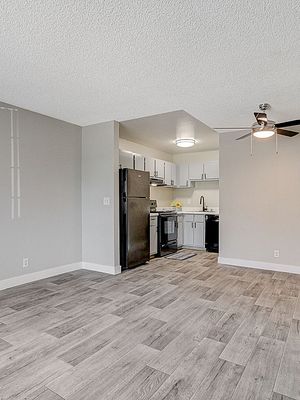 Modern apartment interior with open-concept kitchen and living area, featuring sleek gray flooring and ceiling fan.