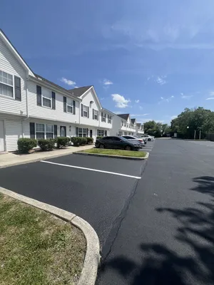 Charming townhouses with white siding and dark shutters, featuring ample parking under a clear blue sky.