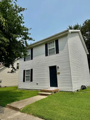 Charming two-story white house with black shutters and a lush green lawn, perfect for families seeking comfort and style.