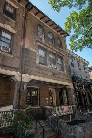 Charming historic brownstone with rustic facade, classic windows, and inviting front porch, set under a clear blue sky.