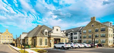 Charming stone-clad apartment complex with ample parking and lush landscaping under a bright blue sky.