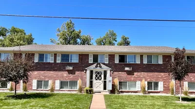 Front view of a classic two-story brick apartment building with green lawn and trees.