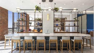 Elegant modern apartment lounge featuring a spacious open-plan layout, sleek countertop bar with stylish stools, and contemporary light fixtures under natural light from large windows.