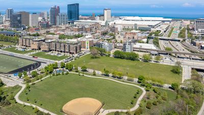 Vibrant cityscape view highlighting modern architecture with a mix of residential and commercial buildings adjacent to lush green park spaces and sports facilities, under a clear blue sky.