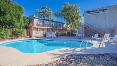 Inviting apartment complex with a pristine pool, surrounded by lush greenery and comfortable lounge seating.