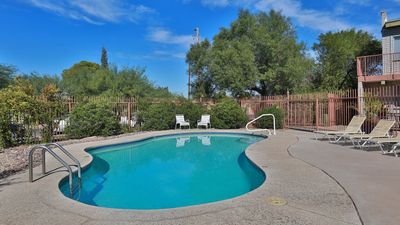 Inviting outdoor pool area with comfortable lounge chairs, surrounded by lush greenery and clear blue skies.