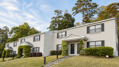 Charming duplex with classic brick exterior, surrounded by lush greenery and a serene environment.