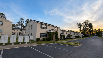 Charming suburban apartment complex bathed in the warm glow of sunset with ample parking and lush greenery.