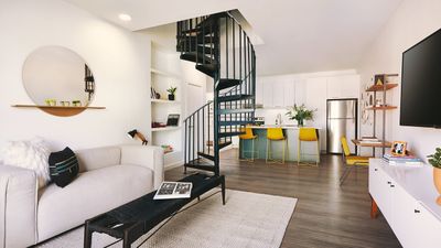 Modern apartment living room with stylish spiral staircase, open-plan kitchen with sleek cabinets, and vibrant seating; perfect blend of contemporary comfort and elegance.