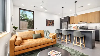 Modern open-concept living room with luxurious brown leather sofa and sleek kitchen island featuring stylish bar stools.