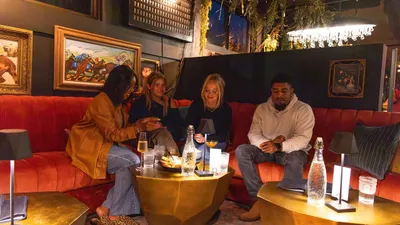 Stylish lounge atmosphere with friends enjoying drinks on a cozy red sofa surrounded by elegant artworks and soft lighting.